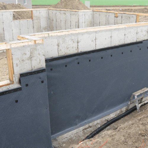 picturing an exterior basement wall with black dimple board - a rigid plastic waterproofing membrane - installed on the exterior of the basement wall to help with basement waterproofing